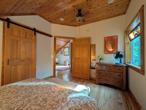 A bedroom with a bed, wooden ceiling, a dresser, a mirror, and a window with a stained glass design. - Bright and spacious, modern carriage house apartment. WiFi. 2 miles from town. (Beaver Island)