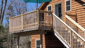 Un pontile in legno con un ombrellone blu, una scala e vista sulla foresta circostante.
