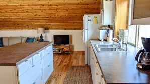 Una cucina compatta con soffitto in legno, mobili bianchi, forno integrato e macchina per il caffè.
