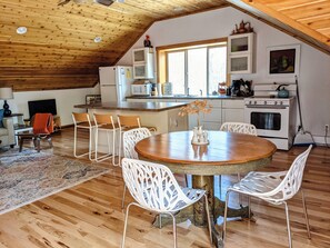A cozy kitchen with a wooden ceiling, white cabinets, and a dining area with a round table and white chairs.