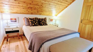 Una camera da letto con soffitto in legno, un letto con copripiumino grigio, due comodini con lampade e una porta in legno.