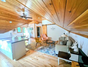 A cozy, wooden-floored room with a kitchenette, a dining area, and a seating space with a ceiling fan.