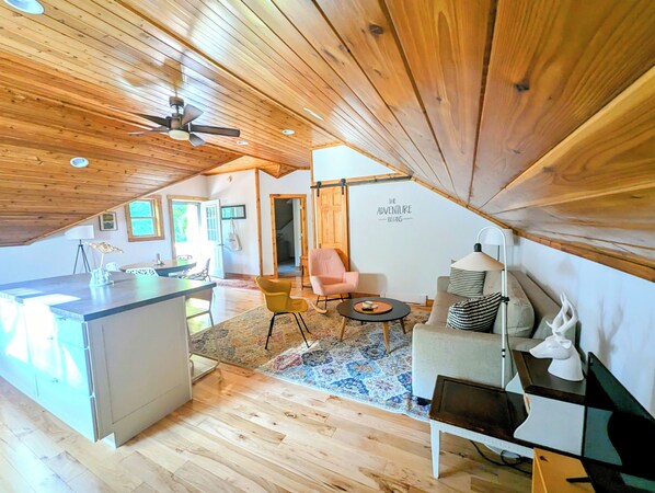A cozy, wooden-floored room with a kitchenette, a dining area, and a seating space with a ceiling fan. - Bright and spacious, modern carriage house apartment. WiFi. 2 miles from town. (Beaver Island)