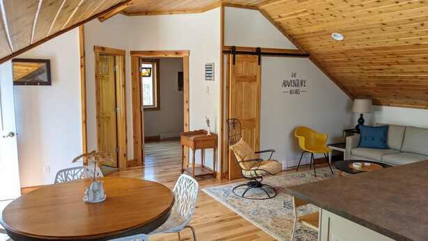 Un ambiente accogliente e luminoso con pavimento in legno, una zona pranzo con tavolo rotondo e sedie bianche, un divano e una ventola a soffitto.