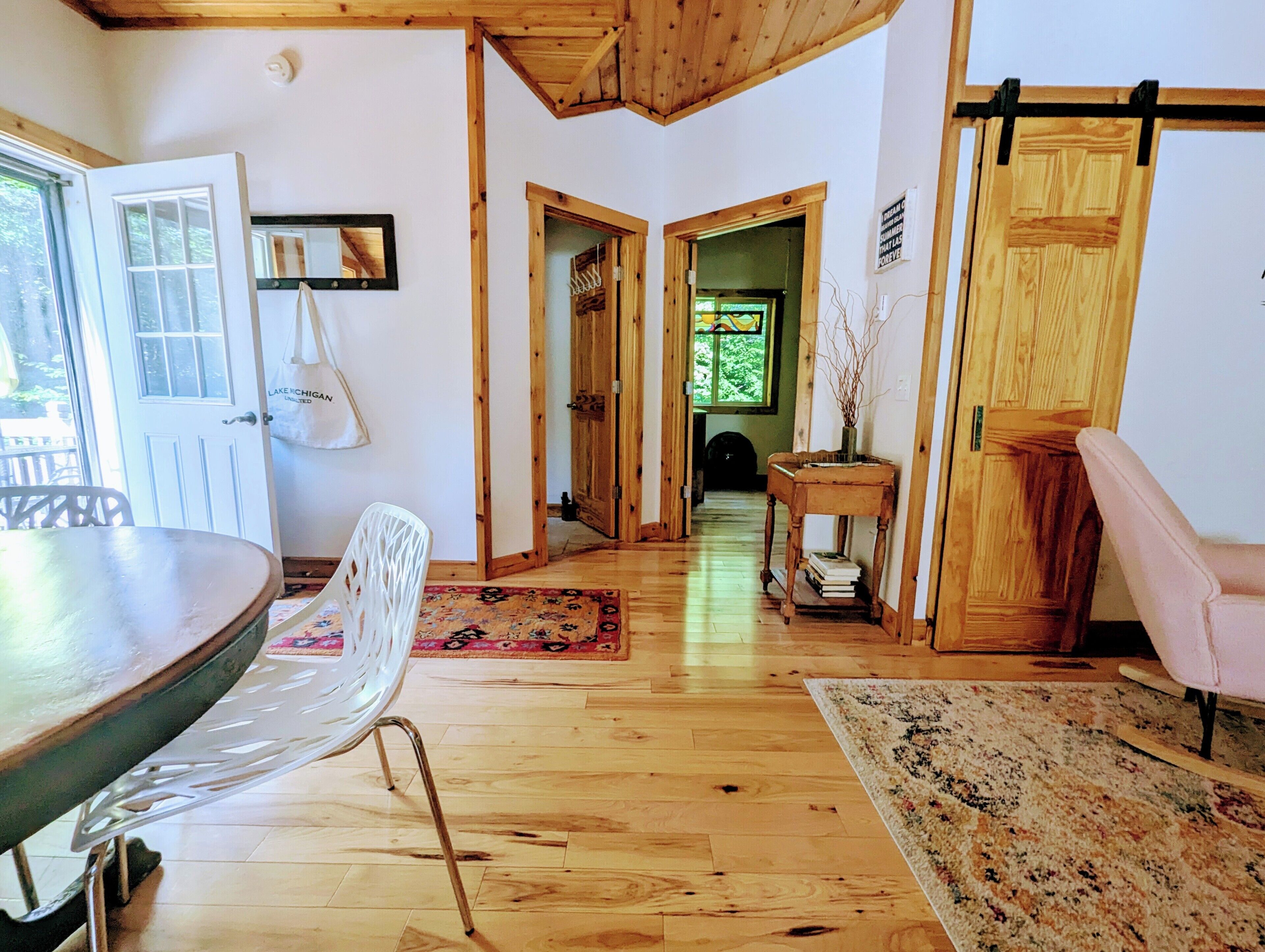 A room with a wooden ceiling, a dining table, a white chair, a wooden door, and a rug.