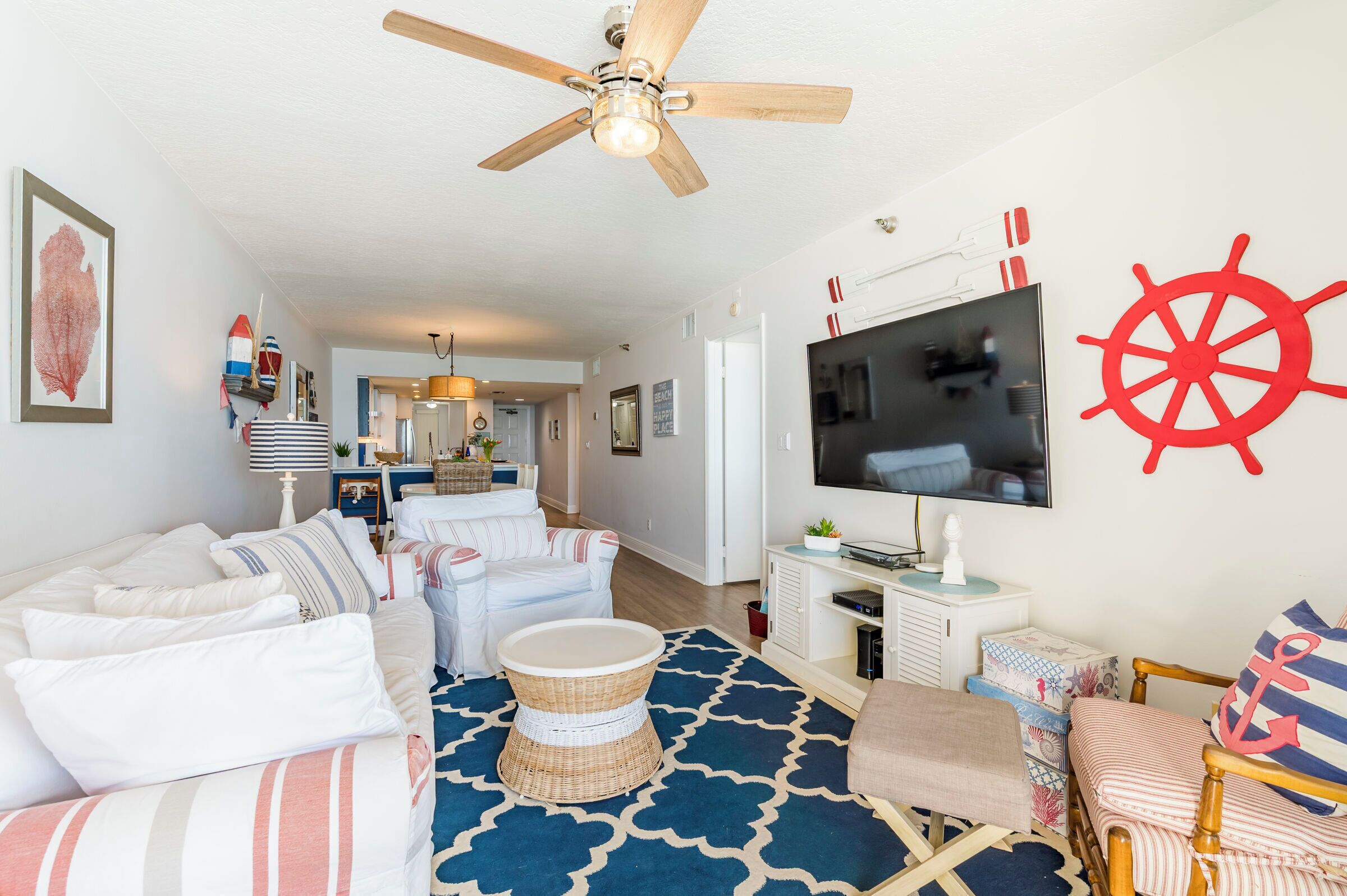 A living room with a ceiling fan, a TV, a large red anchor wall decoration, and a wicker coffee table.