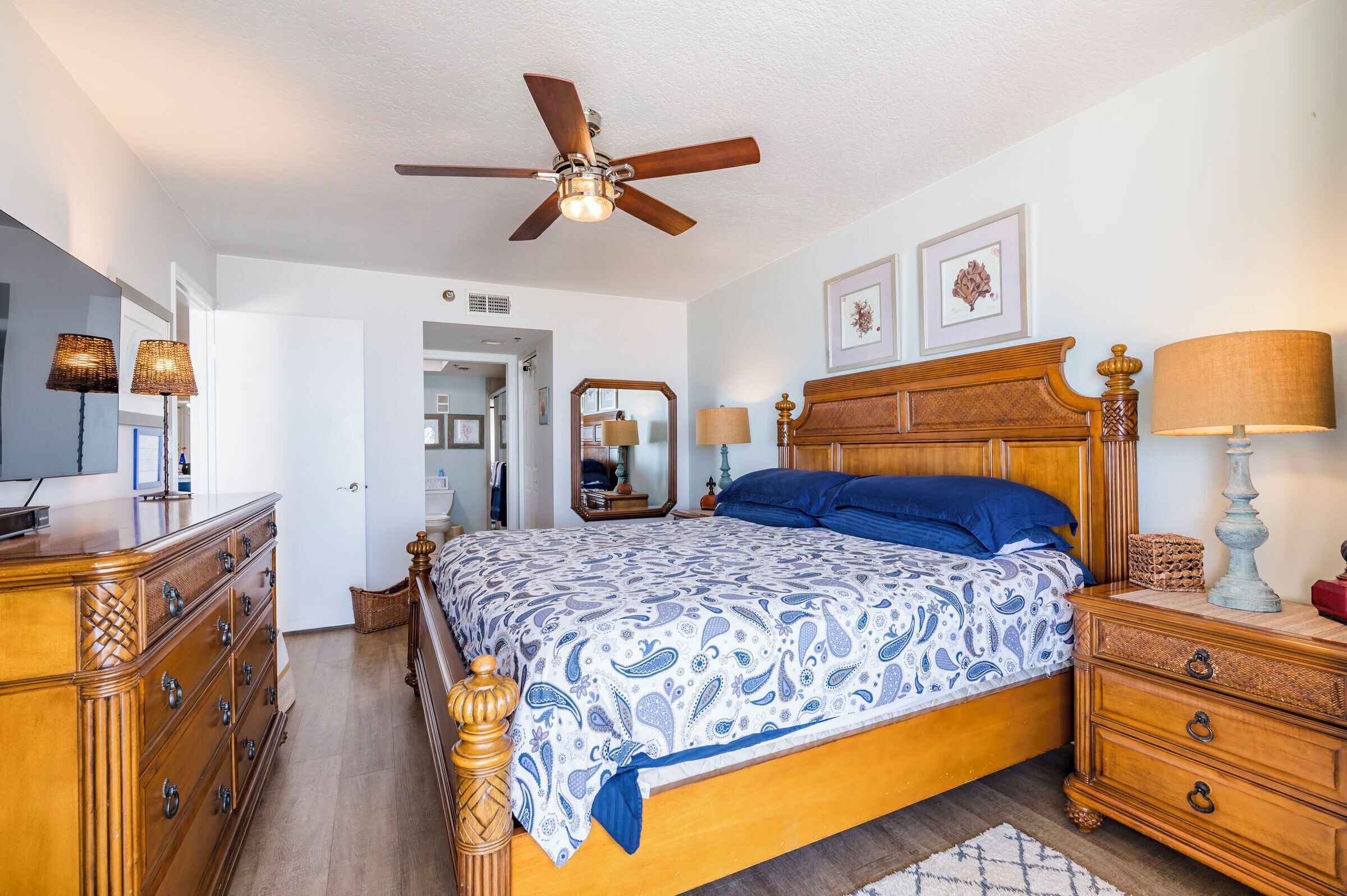 A bedroom with a wooden bed, a ceiling fan, a dresser, and a nightstand.