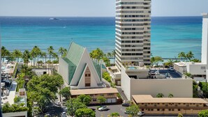 A high-rise hotel with a view of the ocean, palm trees, and a distinctive building with a green roof.