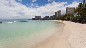 A beach with clear turquoise water, a sandy shore, and tall buildings in the background.
