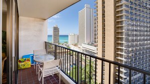 A balcony with a table and chairs, overlooking a cityscape with tall buildings and a view of the ocean.