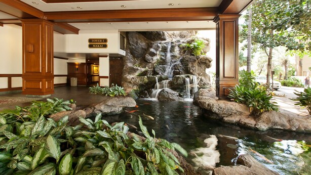 A hotel lobby with a waterfall feature, a reception desk, and a sign indicating 'Tower I Makai'.