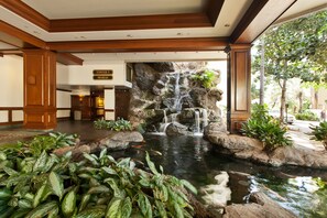 A hotel lobby with a waterfall feature, a reception desk, and a sign indicating 'Tower I Makai'. - Great Ocean View 1 Bedroom, Full Kitchen, (Honolulu)