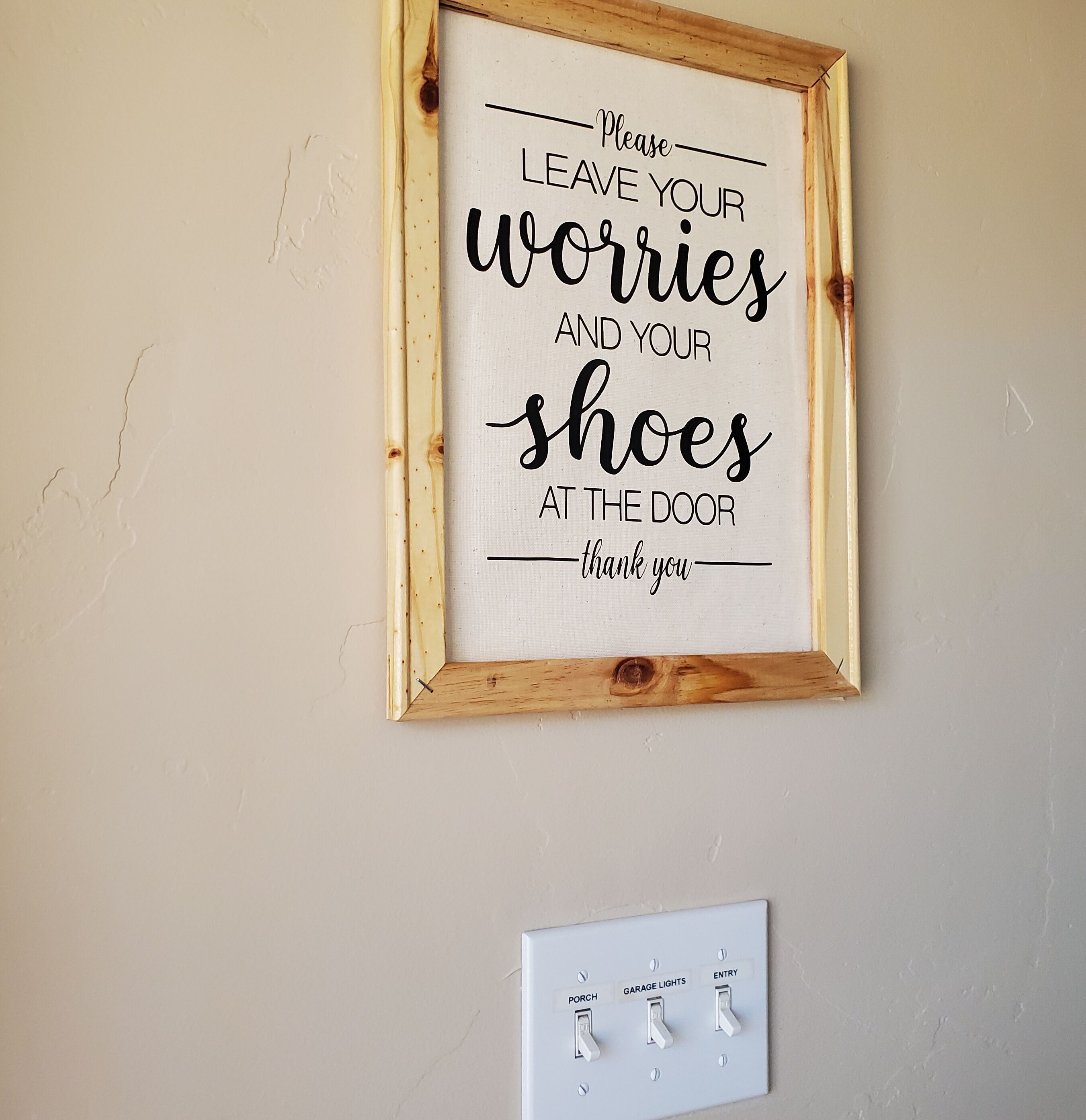 Un cartel enmarco con un mensaje sobre dejar preocupaciones y zapatos en la entrada, y debajo, un panel de interruptores de luz instalado en la pared.