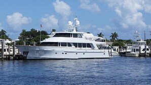 Eine große weiße Yacht liegt in einer Marina, umgeben von anderen Booten, unter blauem Himmel.
