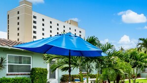 Ein Hotelinnenhof mit blauem Sonnenschirm, Palmen und einem Gebäude im Hintergrund.