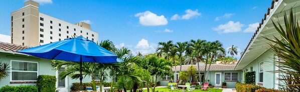 A hotel courtyard with a blue umbrella, palm trees, and a building in the background.