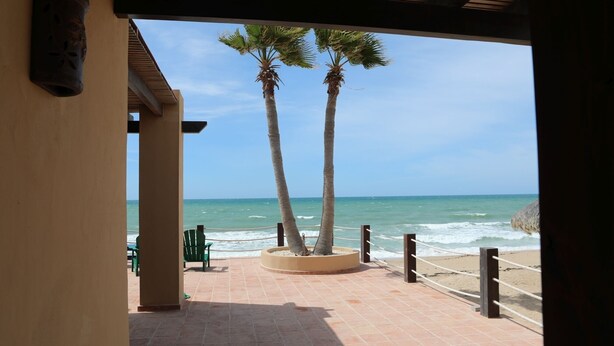 Vista a la playa con palmeras y una terraza de madera.