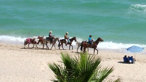 Una playa con gente montando caballos a lo largo de la orilla.