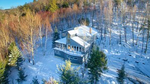 A large, modern house surrounded by a forest with snow on the ground.