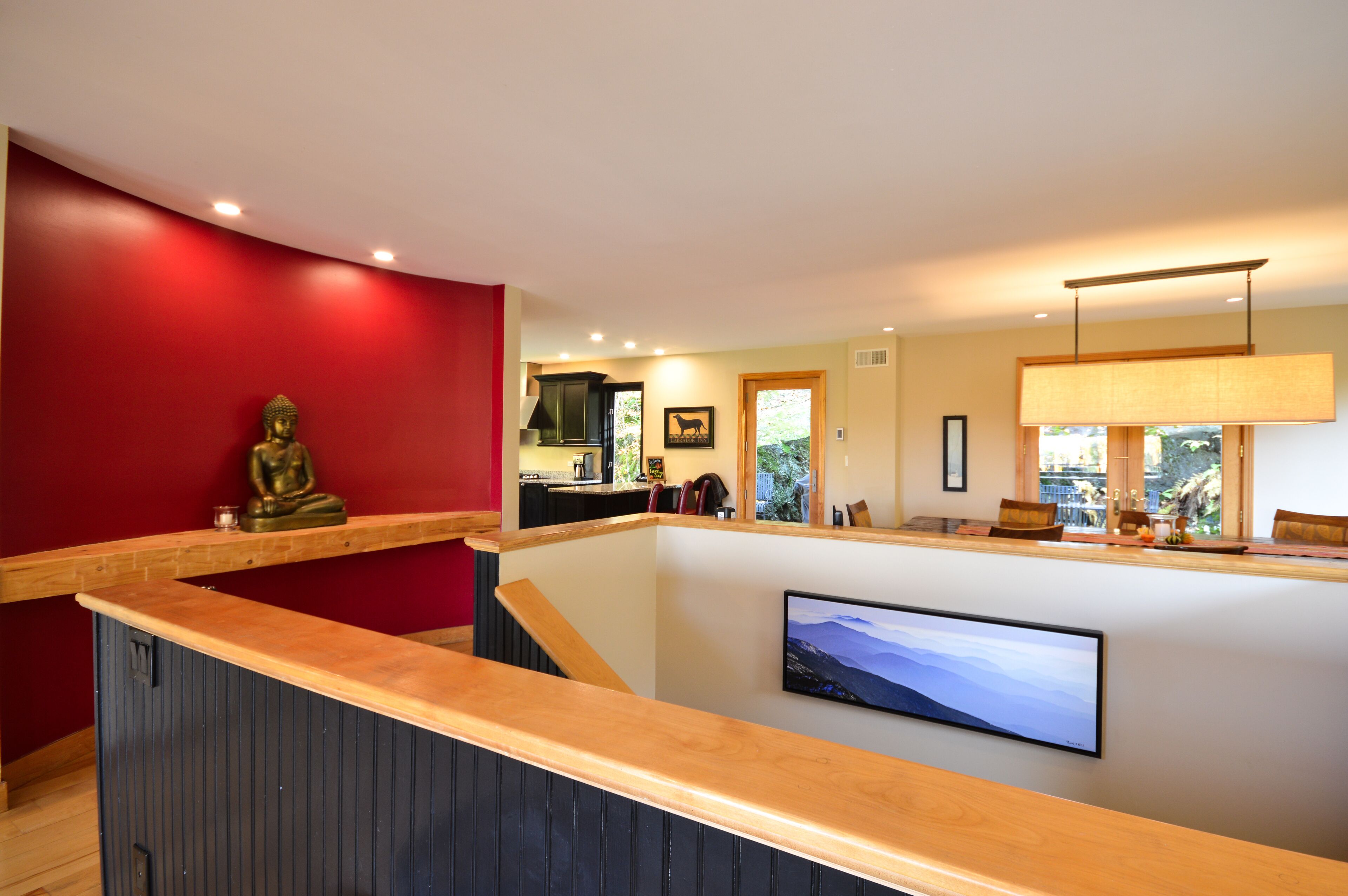 A modern interior with a wooden reception desk, a Buddha statue, a flat-screen TV, and a kitchen area in the background.