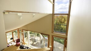 A high-ceilinged room with large windows, a wooden staircase, and a view of the outdoors.