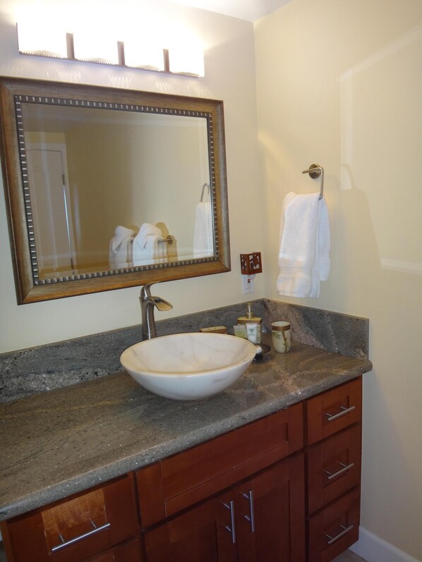 A bathroom with a large mirror, a white vessel sink, wooden cabinets, and a towel hanging on the wall. - Super Luxury, Direct Oceanfront, 20 yards From Ocean, Whale Watchers Paradise (Wailuku)