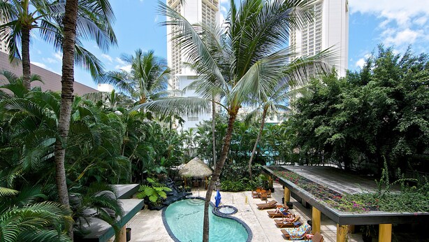 A pool area with lounge chairs, a thatched umbrella, and lush greenery.