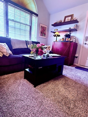 Ein Wohnzimmer mit einer Couch, einem Couchtisch mit Blumen, einer Lampe und einem Bücherregal.