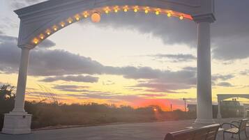 Un banco debajo de un arco blanco con luces, con vistas a la puesta de sol.