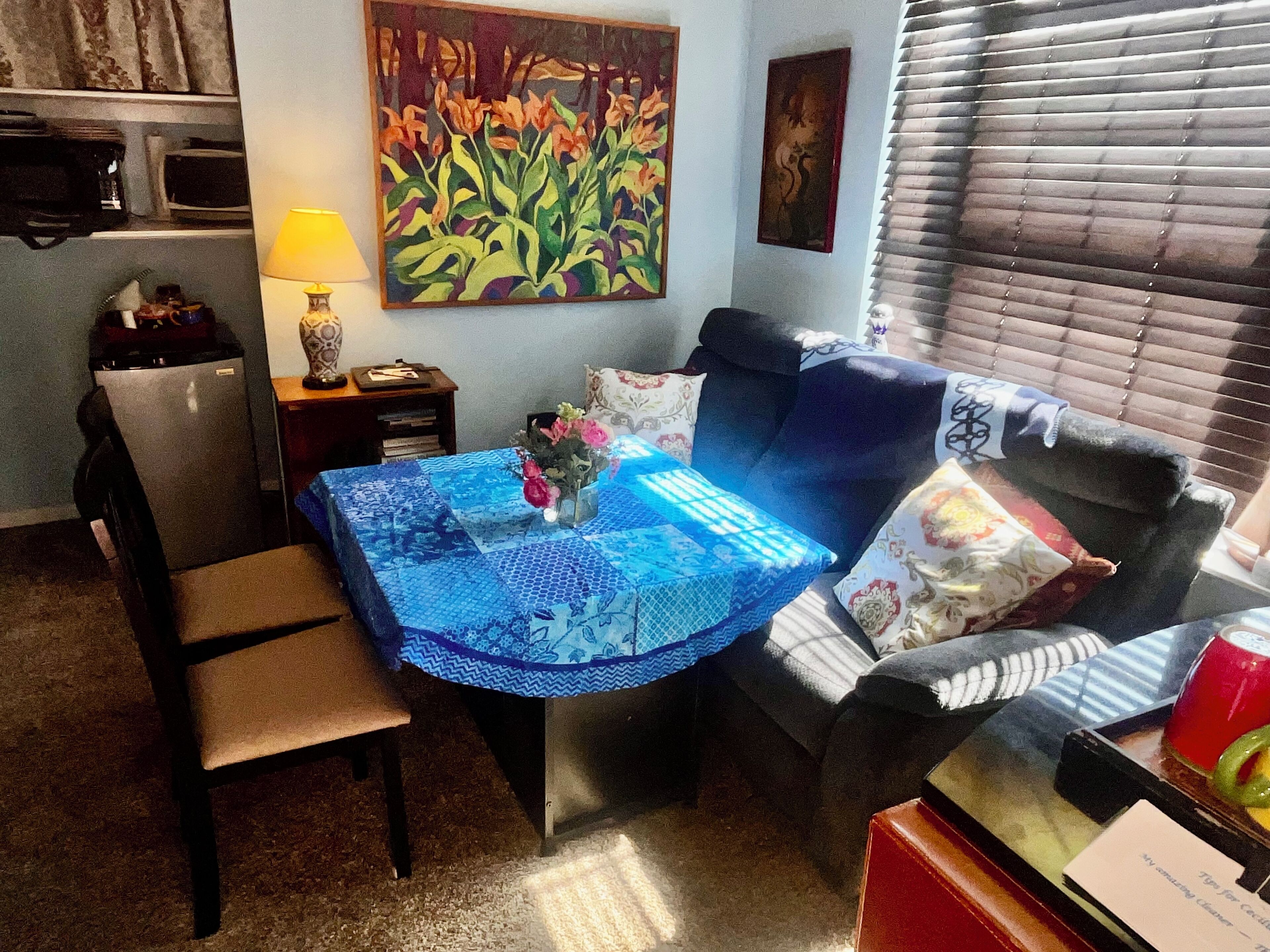 A cozy living room with a blue patterned table, a comfortable sofa, a small table with a red cup, and a painting on the wall.