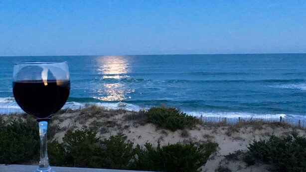 Um copo de vinho tinto sobre uma mesa, com vista para o oceano e uma praia arenosa.