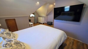A bedroom with a large bed, a TV mounted on the wall, a desk, and a wardrobe. - CLE Garden Retreat, 4-Min to Airport & Metroparks, Ping Pong, BBQ & Private Yard (Cleveland)