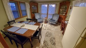 A dining area with a wooden table, chairs, and a patterned rug. There are two windows with curtains, a ceiling fan, and a refrigerator. - CLE Garden Retreat, 4-Min to Airport & Metroparks, Ping Pong, BBQ & Private Yard (Cleveland)