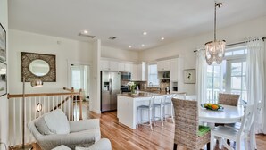 A spacious living area with a dining table, wicker chairs, and a kitchen in the background. - Gulf Front Pool + Bikes! South of 30A, Steps to Beach, between Alys & Rosemary (Seacrest Beach)