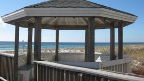 Ein hölzerner Pavillon mit weißem Dach und offener Bauweise, der auf einen Strand mit Sand und Meerblick blickt.