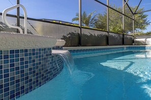 A swimming pool with a tiled edge, a small waterfall feature, and a view of palm trees through a covered area. - Movie Magic House - Southern Pool, Themed Rooms! (Kissimmee)