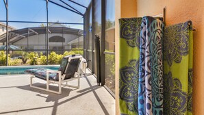 Un espace extérieur abrité comprenant une piscine, un fauteuil de relaxation et des rideaux à motifs.