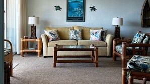 A living room with a beige sofa, two side tables with lamps, a wooden coffee table, and a ceiling fan. - Panoramic Ocean and Sunset View in Poipu – Enjoy Lofty Haven Cross-Breezes! (Koloa)