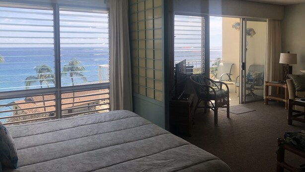 A hotel room with a bed, a desk, and a view of the ocean. - Panoramic Ocean and Sunset View in Poipu – Enjoy Lofty Haven Cross-Breezes! (Koloa)