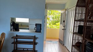 A compact living space with a kitchenette, a bench, a wicker shelf, and a view of the outdoors. - Panoramic Ocean and Sunset View in Poipu – Enjoy Lofty Haven Cross-Breezes! (Koloa)