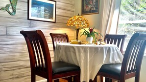 A dining area with a wooden table, four chairs, a decorative lamp, and two framed pictures on the wall.
