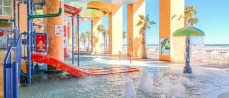 An indoor water park with slides, water jets, and palm trees.
