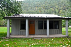 A small, single-story building with a porch, a front door, and large windows. - Cozy and relaxing, Modern Creekside, Trailside, Waterfront Cottage, fiber Wifi (Cammal)