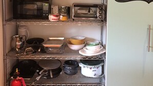 Una cocina con estantes que contienen platos, vasos y un microondas. Hay una pizarra con un mensaje de bienvenida.