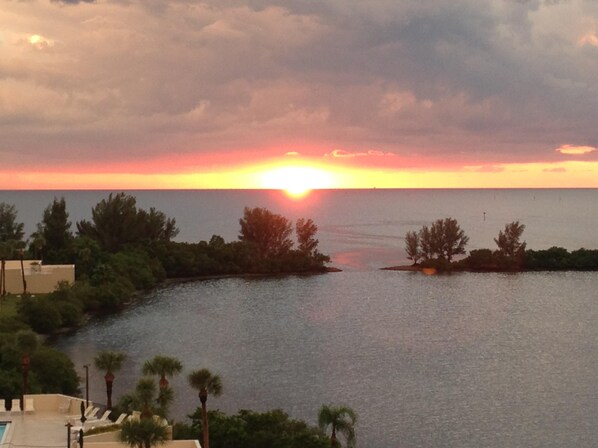 A sunset view over a body of water with trees and a building in the foreground.