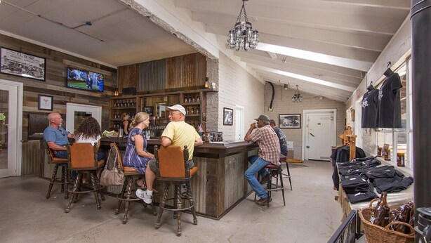 Uma área de bar com banquetas de madeira, um balcão e uma televisão fixada na parede.