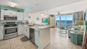 Una cocina moderna con una isla central, un comedor con vistas y una sala de estar con sofá y televisor.