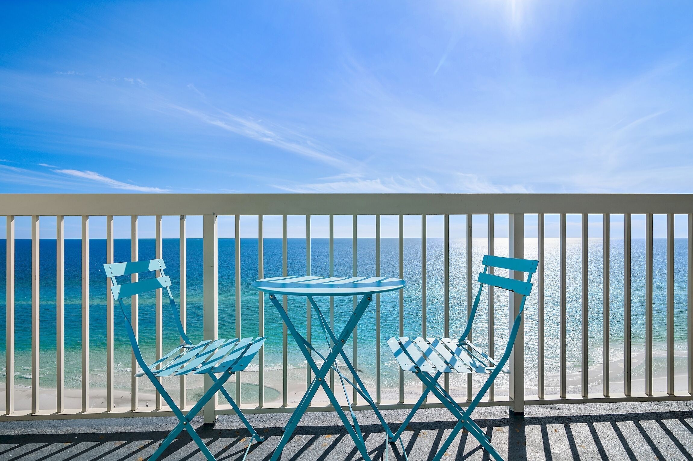 A balcony with a view of the ocean, featuring two blue folding chairs and a small round table.