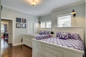 Two beds are dressed in patterned bedding, surrounded by framed pictures and a window with blinds.