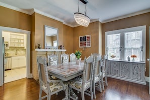 Traditional dining room with a wooden dining table and six chairs, a chandelier, and a kitchen in the background.